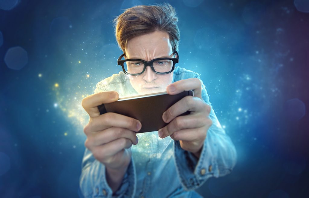 A young man wearing glasses looking at his phone intensely